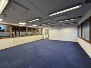 Empty office space with blue carpet, white walls, and large windows at De Ruijterkade.